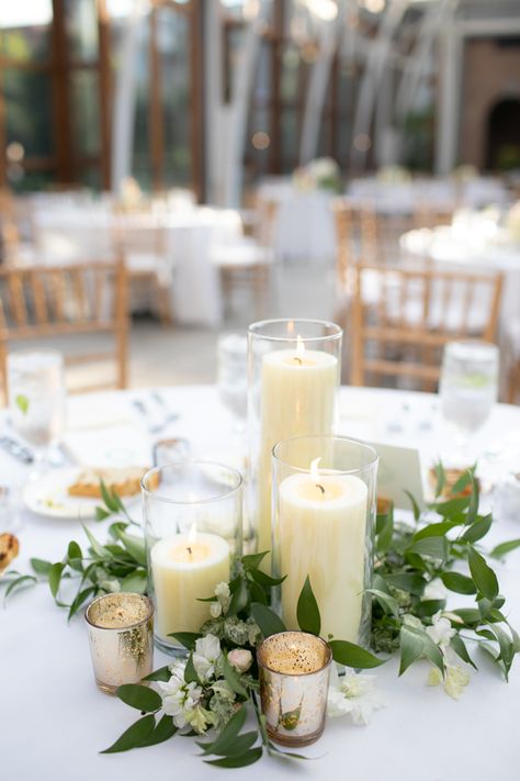 Candle Centerpiece at Romantic Orangerie at Tower Hill Botanic Garden Massachusetts Wedding #weddings #wedding #weddingplanning #weddingflowers #floraldesign Greenery And Candles Centerpieces, Candle Floral Arrangements, Candle With Greenery Centerpiece, Wedding Pillar Candle Centerpieces, Wedding Table Pillar Candles, White Flower Candle Centerpieces, Candles And Greenery Centerpiece Round Table, Floral And Candle Centerpiece Wedding Round Table, Wedding Candle Arrangements