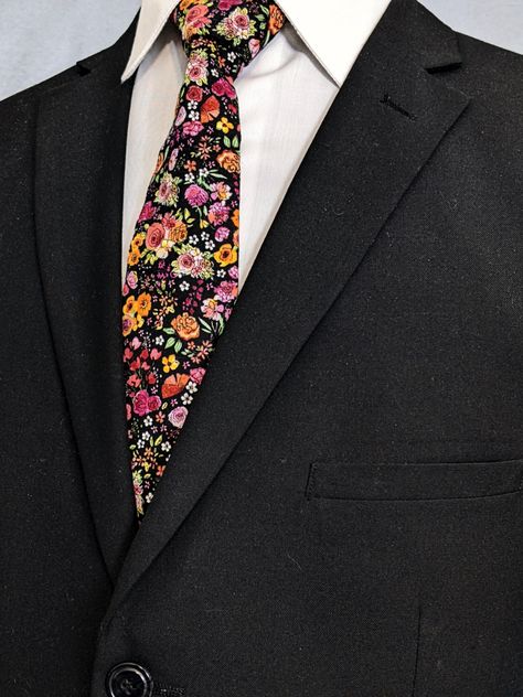 Men's colorful necktie. Features a black background with a small floral print. Colors include shades of reds, golds, oranges, pinks, greens, white and black. #Floral #Wedding #Necktie #Flower #Black Floral Ties For Men, Black Suit Floral Tie, Floral Suit Men, Enby Fashion, Garden Outfit, Black Pocket Square, Connie Baby, Winter Shoot, College Wardrobe