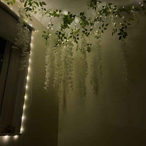 Celling decorated with white wisteria flowers and fairy lights. Night time. Vines And Fairy Lights Hanging From Ceiling, Ivy Fairy Lights Living Room, Bedroom Decor Ideas Fairy Lights, Bedroom Ceiling Ideas Diy Fairy Lights, Vine Lights On Ceiling, Wisteria Corner Bedroom, Wisteria On Ceiling Bedroom, Hanging Flower Vines, White Wisteria Bedroom Decor