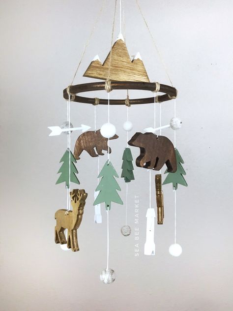 "This woodland crib mobile is one of my favorite designs. The mobile has everything to perfectly tie together a woodland, lumberjack, or camping themed nursery. The mobile comes complete with a snow capped mountain, two bears, two deers, four pointy trees, four modern arrows, four heather grey wool balls and four white wool balls. The colors perfectly contrast each other and are warm and inviting! The hanger is jute twine to tie together the perfect woodland look. Each piece is carved, hand sand Mountain Outdoor Theme Nursery, Woodland Nursery Furniture, Tree Theme Nursery, Cabin Nursery Theme, Mountain Baby Nursery, Camping Themed Nursery, Adventure Nursery Theme, Outdoor Themed Nursery, Outdoorsy Nursery