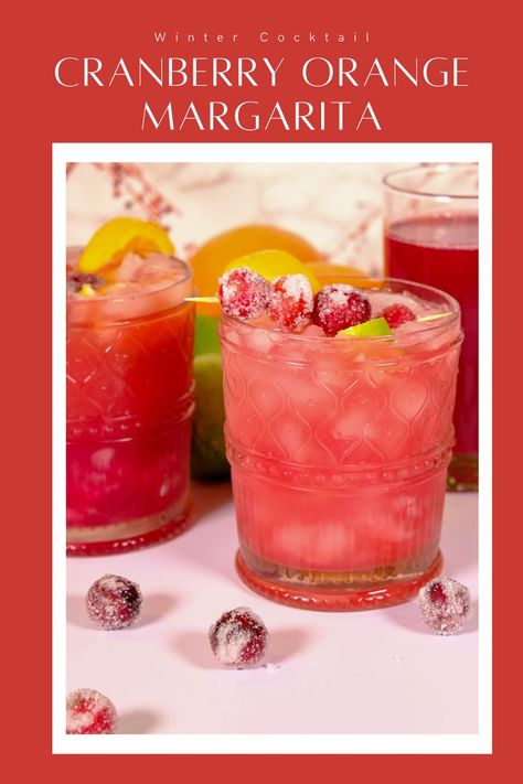 Glass filled with a cranberry orange margarita with sugared cranberries and lime slices as the garnish. Cranberry Orange Margarita Sangria, Frozen Cranberry Margarita Recipe, Pitcher Cranberry Margaritas, Cranberry Margaritas For A Crowd, Cranberry Orange Juice Cocktail, Cranberry Pomegranate Margarita, Orange Cranberry Drink, Cranberry Orange Alcoholic Drinks, Cranberry Orange Drinks Alcohol