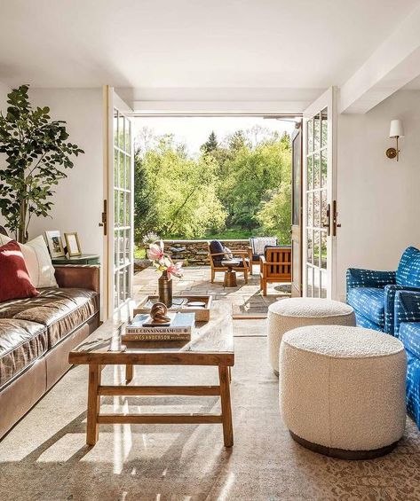 Living room features a brown leather sofa with salvaged wood coffee table and round ivory boucle stools and double doors that lead to a patio. 1920s Farmhouse, Sitting Ideas, Brown Leather Furniture, Party Barn, Brown Leather Sofa, Keeping Room, Home Addition, Lounge Design, Ideas Living Room