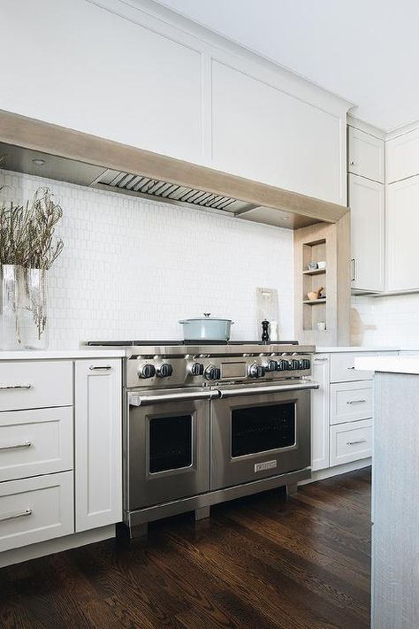 An extra-long light gray wooden range hood is fixed over oak built-in spice racks and above a stainless steel dual range mounted against white oblong cooktop tiles and flanked by light gray cabinets. Ann Sacks Backsplash, Wooden Range Hood, Light Grey Kitchen Cabinets, Kitchen Cooktop, Light Gray Cabinets, Ann Sacks, Modern Farmhouse Kitchen, White Shaker Cabinets, White Kitchen Island