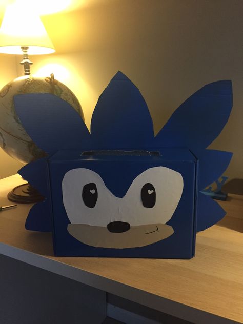 Sonic Valentine's Card Box Idea.  We cut out his hair on a separate piece of cardboard; then spray painted the shoe box and cardboard hair. Eyes, mouth and nose are all just construction paper glued on with a marker smile.  His hair is hot clued to back of the box; with the face on the front.   Turned out SUPER cute! Kids Valentine Shoe Box Ideas, Pre K Valentine Box Ideas For Boys, Decorating Shoe Boxes For Valentines, Diy Valentine's Box For Boys, Valentines Box Ideas Creative Boys, Valentines Day Shoe Box Ideas For Boys, Cool Valentines Boxes For Boys, Sonic Hedgehog Valentine Box Ideas, Sonic Valentine Box Ideas