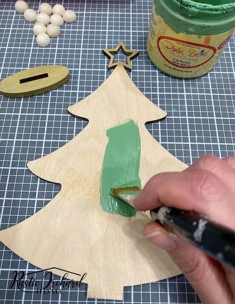 Make your own Wood Christmas Tree Décor with this simple holiday crafting idea! Prek Christmas Tree Crafts, Paint A Christmas Tree On Wood, Simple Wooden Christmas Tree, Painting Wood Christmas Trees, Painting A Christmas Tree On Wood, Tree Shaped Ornaments Diy, Dollar Tree Wood Christmas Crafts, How To Paint A Christmas Tree On Wood, Painting Wooden Christmas Trees