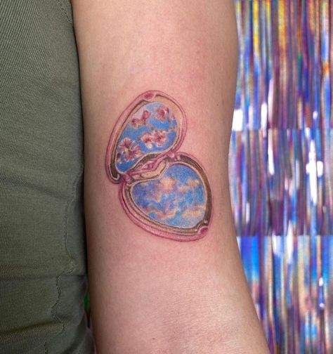 tattoo of heart shaped compact mirror with a reflection of peach blossoms and pastel colored clouds, on bicep of left arm Compact Mirror Tattoo, Cinderella Slippers, Mirror Tattoo, Micro Realism, Mirror Tattoos, Sisters Tattoo, Realism Tattoos, Cinderella Slipper, Gold Tattoo