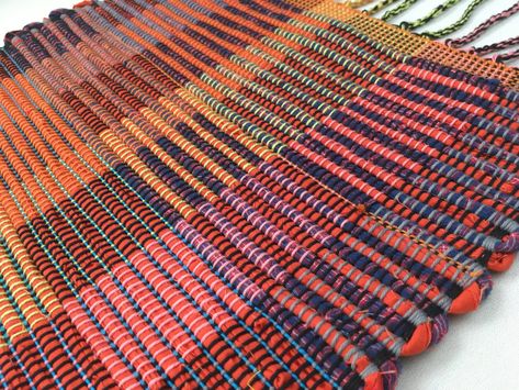 Handwoven wall hanging in shades of red blocks and stripes patterning. Woven on a floor loom in traditional weaving style with all new cotton fabric. Mounted with maple wood top hanger. Made with cotton yarns. Size: 14" x 25" including 6" braided fringe.