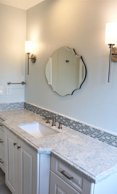 Family bath has a vanity with deeper sink base cabinet for more storage space in the narrow bathroom. Sconce lighting were placed on either side of her elegant mirror. Decorative tile was the backsplash that compliments her vibrant countertop Backsplash For Vanity, Bathroom Vanity Backsplash Ideas Tile, Tile Vanity Backsplash, Bathroom Vanity Tile Backsplash, 1950s Remodel, Bathroom Vanity Backsplash Ideas, Vanity Backsplash Ideas, Tile Backsplash Bathroom Vanity, Lakehouse Bathroom