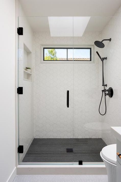 Spacious floor lever shower features white puzzle tiles with a matte black shower kit, a shower skylight and black hexagon shower floor tiles. Black Tile Shower Floor, Shower Black Floor White Walls, Hexagon Shower Floor Tile, Black Hexagon Shower Floor, White Marble Shower With Black Floor, White Tile Bathroom Floor, Marble Tile Shower Walls Black Floor, Shower Skylight, Black Hex Shower Floor