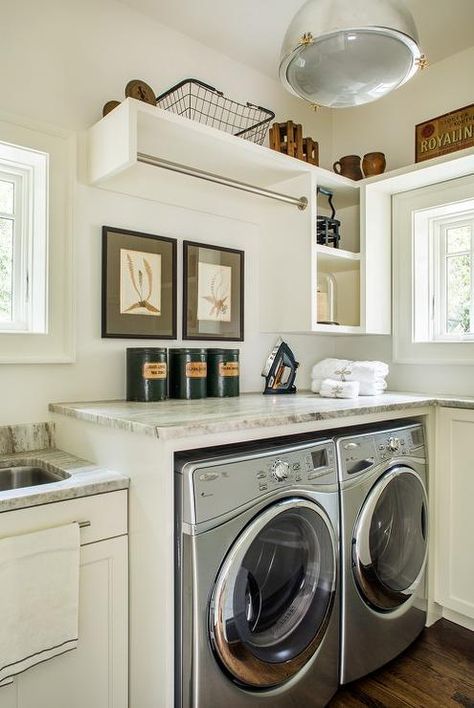 Classic cottage laundry room features a white and gray granite countertop positioned over a silver front loading washer and dryer enclosed beside ivory cabinets lit by a silver pendant. White And Gray Granite, Cottage Laundry, Cottage Laundry Room, Laundry Room Counter, Laundry Room Countertop, Grey Laundry Rooms, Green Laundry, Pantry Laundry Room, Gray Granite