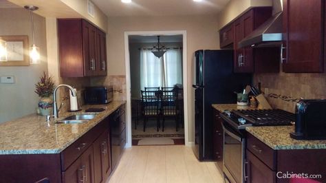 This beautiful galley kitchen transformation uses Shaker Cherry Java cabinets, light colored granite countertops, and stainless steel appliances. Tile With Cherry Cabinets, Kitchen Remodel Cherry Cabinets, Kitchen Hardware Cherry Cabinets, Schuler Cabinets Cherry Cappuccino, Kitchen Island Table Combination, Galley Kitchen Cabinets, Java Stain, Modern Cherry Cabinets Kitchenhoodtips In Cherry Kitchen, Framed Cabinets