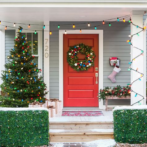 Dress up a traditional front porch and entry using all the classic Christmas decorations. Hang multicolor string lights, pin a stocking to a mailbox, decorate a Christmas tree and hedges with lights and lighted faux presents, add greenery and a door wreath and put down a new holiday welcome mat. Porch Christmas Lights, Christmas Lights Outdoor Trees, Multi Colored Christmas Lights, Christmas Porches, Colored Christmas Lights, Christmas Door Decoration, Front Door Christmas Decorations, Christmas House Lights, Classic Christmas Decorations