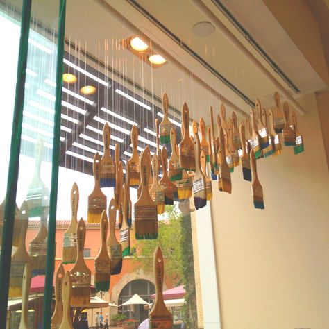 Hanging paintbrushes in a kids' art studio Art Gallery Store Design, Painting Store Windows, Art Gallery Window Display Ideas, Art Studio Retail Space, Art Shop Display Ideas, Art Retail Store, Art Gallery Window Display, Retail Signage Instore Display, Paint Display Ideas Retail