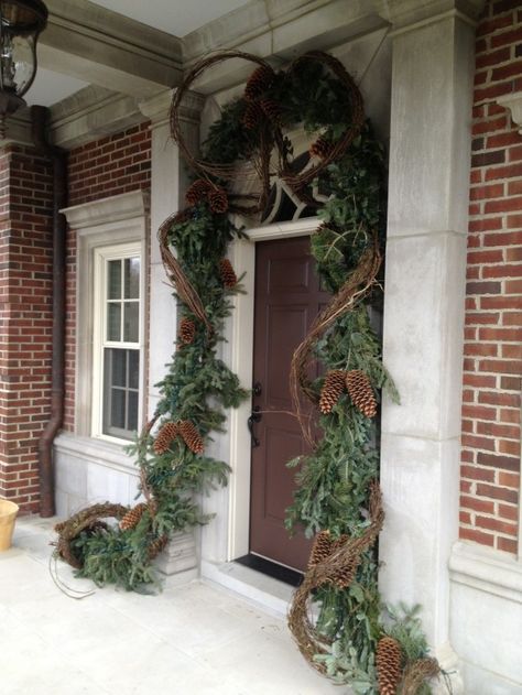 Christmas front door & entry decor - evergreen garland, grapevine, large pinecones, lights Grapevine Christmas Garland, Grapevine Garland Front Door Christmas, Decorating With Grapevine Garland, Grapevine Garland Ideas, Grapevine Garland Front Door, Front Porches Farmhouse, Brick Entryway, Evergreen Garland, Grapevine Garland