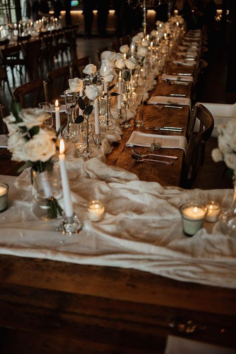 Cosy and luxe wedding tablescape for a rustic wedding with all-white touches including a white table runner, white candles, and white rose arrangements Beige Table Runner Wedding, Hidden River Cabins Wedding, Long Rustic Dining Table, White Table Runner Wedding, Brown Wedding Cakes, Wedding Candles Table, Wedding Table Setup, Wedding Runner, Wedding Cake Pearls