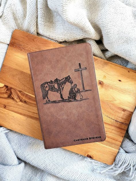 For the Christian cowboy in your life- check out this praying cowboy leather Bible by Ross Paint Shop! The personalized Bible comes in several versions, including NIV, ESV, NLT, KJV, and NKJV, and it shows a horse and praying cowboy next to a cross. Head to the shop to get your own cowboy Bible or check out our other horse and western designs! Esv Single Column Journaling Bible, Cowboy Praying, Niv Journaling Bible, Pocket Bible, Bible Design, Esv Study Bible, Ranch Gifts, Esv Journaling Bible, Painted Bible