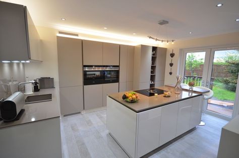 The tall bank of recessed kitchen units create a real wow factor adding to the minimalistic, uncluttered look of the kitchen. We used LED lighting above the units to enhance and highlight them. Lit Up Kitchen Island, Lighting Above Kitchen Cabinets, Bank Of Tall Kitchen Units, Kitchen Peninsula With Hob, Gloss Cashmere Kitchen, Kitchen Island Induction Hob, Penthouse Kitchen, Tall Unit, White Kitchen Cupboards