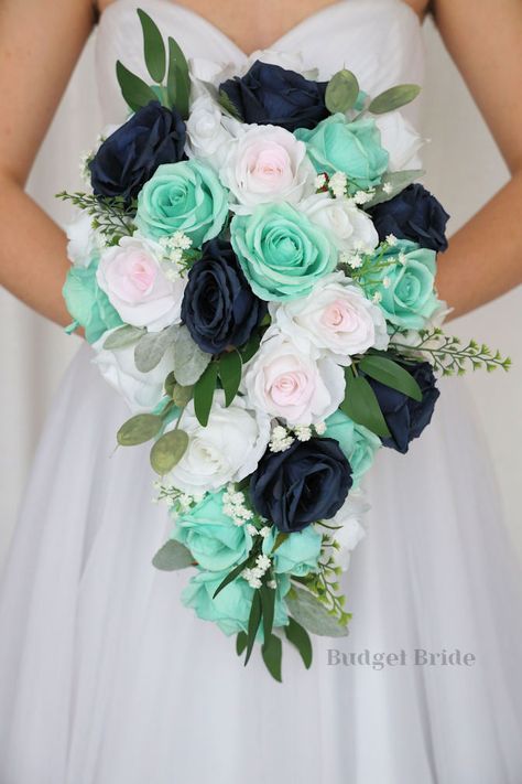 This lovely assortment of navy blue, blush pink and mint green roses is bound to turn heads on your wedding day. This lovely cascading brides’ bouquet from the is an absolutely breathtaking arrangement for any bride to be, in any season. Sage greenery and white accents complete the look and add a delicate realism to this beautiful bouquet. This bouquet is 10” wide, 18” long, and is crafted by our in-house florists without using a foam base to anchor the flowers to the bouquet. Instead, we wire o Mint Green And Blue Wedding, Teal And Mint Green Wedding, Mint Green Flowers Bouquet, Navy And Mint Wedding, Seafoam Wedding, Navy Blue Bouquet, Turquoise Bouquet, Small Bridesmaid Bouquets, Fake Wedding Flowers