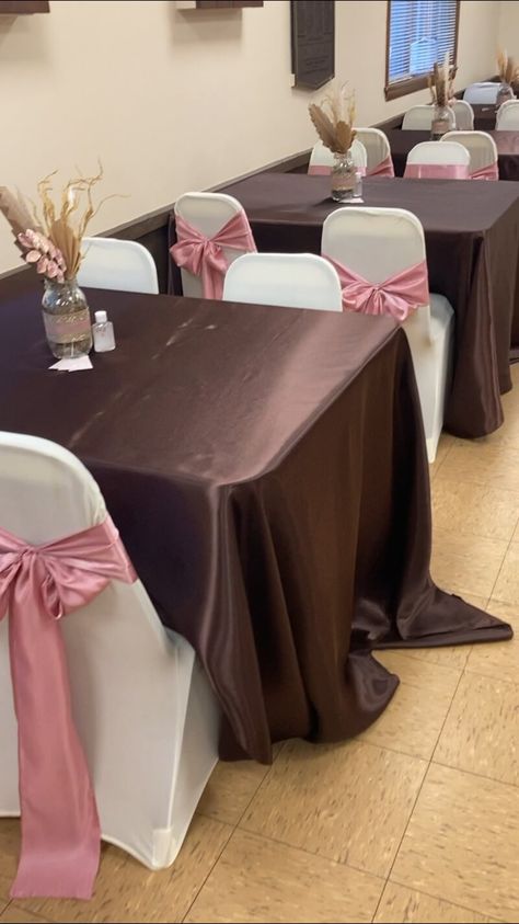 Accentuate your festive event decor by draping the party tables with chocolate brown satin tablecloths. Flaunt pretty flowers and sprays in glass vases embellished with rhinestone ribbons to exude a lovely floral vibe. Moreover, adorn the chairs with white covers and pink sashes elevating the elegance of your overall setup up a notch. Pink Party Tables, Event Decor Ideas, Party Decorations Table, Party Tables, Party Table Settings, Decorations Table, Brown And Pink, Brown Satin, Festive Tables