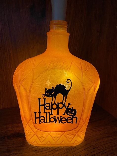 "This accent lamp is a great way to decorate for Halloween! It is a cleaned, repurposed liquor bottle that has been painted orange and decorated in high quality vinyl with a cat wishing a Happy Halloween on one side and a witch enjoying a moonlit ride on the other side.  It is lit with a strand of battery operated lights. The batteries are housed inside the \"cork\" and are easily changed when necessary." Liquor Bottles Crafts, Halloween Bottles And Jars, Repurposed Liquor Bottles, Halloween Bottle Crafts, Crown Royal Bottle Crafts Diy Halloween, Halloween Decorations Bottles, Repurpose Liquor Bottles, Halloween Liquor Bottles, Halloween Bottle Art