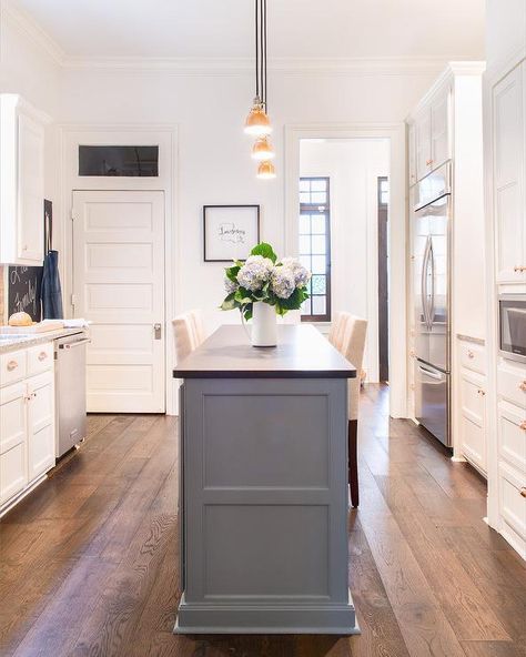 Cream upholstered counter stools flank a slim gray kitchen island topped with a black leathered granite countertop illuminated by three brass mini industrial pendants. Black Leathered Granite, Kitchen Island Granite, Gray Kitchen Island, Marble Top Kitchen Island, Upholstered Counter Stools, Leathered Granite, Kitchen Island With Granite Top, Narrow Kitchen Island, Top Kitchen Designs