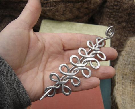 We designed, hammered and twisted 9 gauge aluminum wire to handmake this unique Celtic knot inspired hair barrette pin or shawl pin. Aluminum makes it a lot lighter than it appears. Really! We smoothed all the edges so that it will not catch on your shaw or hair. The pin measures about 3 7/8- 4 1/2 (9.9 - 11.5cm) long and about 1 1/4- 1 1/2 (3.2 -3.8 cm) across the widest part. The stick pin part with the spiral on top that slips through the main design to secure the pin is about 5 1/8- 6 (1... Diy Wire Hair Pin, Hair Pin Silversmith Instructions, Diy Wire Shawl Pin, Blacksmith Hair Pin, Celtic Shawl Pins, Celtic Braid, Celtic Hair, Scarf Pin, Modernist Jewelry