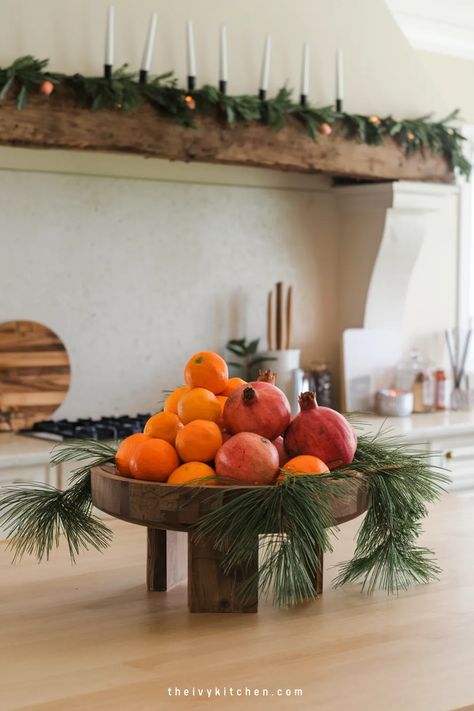 Festive kitchen display with oranges and pomegranates on a wooden stand, adorned with evergreen branches. Kitchen Island Christmas Decor, Island Christmas Decor, Kitchen Island Christmas, Ivy Kitchen, Christmas Kitchen Decor Ideas, Pretty Decorations, Farmhouse Vibes, Kitchen Shelf Decor, Above Kitchen Cabinets