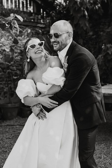 Groom wearing sunglasses hugs the bride from behind in a puff sleeve wedding dress with white sunglasses Bride White Sunglasses, Sunglasses With Wedding Dress, Wedding With Sunglasses, Wedding Pictures With Sunglasses, Wedding Pictures With Glasses, Bride And Groom Sunglasses Photo Ideas, Bride With Sunglasses Photo Ideas, Bridal Party With Sunglasses, Wedding Dress Sunglasses