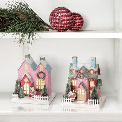 Immerse yourself in timeless charm and festive cheer with a 10" Led Cardboard Village House Set of 2. These charming houses exude warmth and coziness, perfect for creating a festive atmosphere in your home. Each house is meticulously crafted from durable cardboard and adorned with intricate details such as cotton snow, bottle bristle trees, wreaths, garlands adorned with glossy ornament balls, and a white picket fence. Led warm white lights emit a soft glow and can be seen throughout the front w Putz Houses Display, Christmas Houses Village, Cardboard Village, Holiday Village Display, Christmas Nutcrackers, Warm White Lights, Christmas Houses, Christmas Village Houses, Glitter Houses