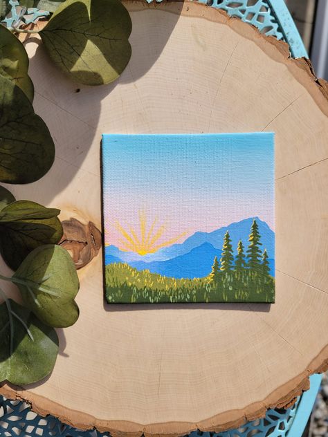 This original, hand-painted piece is a mini landscape scene painted in bright blues, forest greens, and a touch of sunny yellow. It was inspired by the crisp morning air and bright rays of sunshine you experience at sunrise in the mountains. This piece makes a great gift for your partner, friend, coworker, sibling, parent, or just for yourself! Display it on your desk at the office, on your dresser in your room, or on the wall in any room in your home. *Original Acrylic on Canvas Board *Title: Kruger Rock Sunrise *Size: 4in x 4in *Signed on back *Unframed *Mini easel available for add-on purchase *Shipped with tracking and wrapped for protection *Please note: colors may vary slightly from pictures depending on the screen you view the product on If you are not pleased with your purchase, no 2 Inch Canvas Paintings, Cute Square Canvas Paintings, Outdoors Painting Ideas, Mountain Simple Painting, Small Nature Paintings, Canvas Painting Western, Paintings For Your Best Friend, Canvas Landscape Painting Acrylics, Nature Painting Ideas Easy