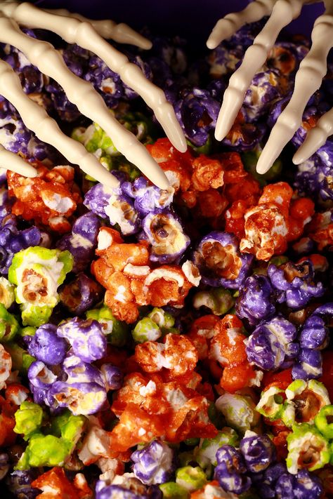 A bowl of orange, lime green, and purple glazed halloween popcorn, with plastic skeleton hand serving forks on top. Doce Halloween, Halloween Popcorn Mix, Jello Popcorn, Gluten Free Halloween Food, Jello Flavors, Halloween Popcorn, Popcorn Mix, Purple Food Coloring, Popcorn Snacks