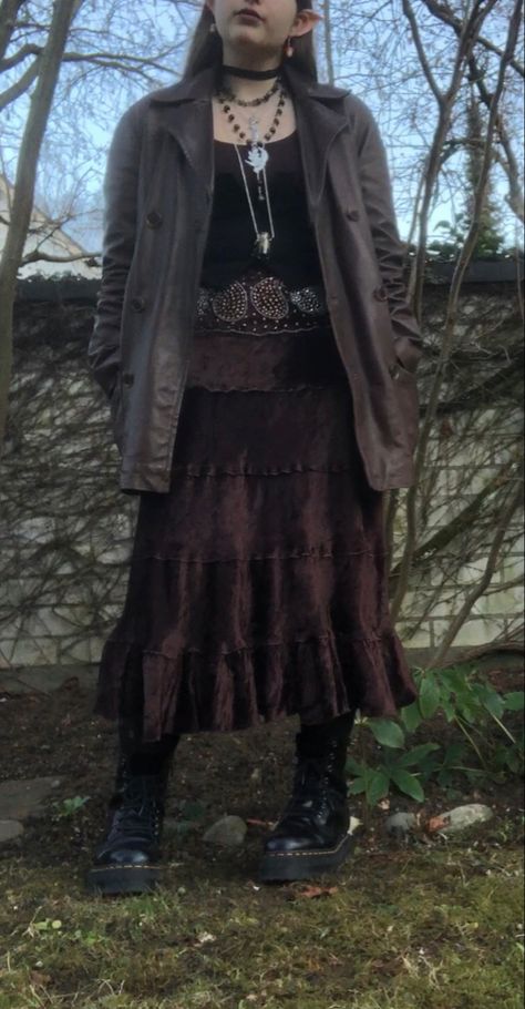 A mid-size person/girl wearing mate rose lipstik, a black tight waistcoat with a ripped stocking selfmade longsleeve and a thrifted dark brown maxi skirt, black dr. Martins and multiple crystal rings and bracelets. 	The person is also wearing multiple silver necklaces, one in form of a dragonfly and another in form of a moon, a green crystal bead necklace and a black lace choker. Dark Witchy Outfits Aesthetic, Dark Forest Core Outfit, Dark Fairycore Costume, Woodland Goth Aesthetic Outfits, Black Maxi Skirt Outfit Goth, Autumn Fairycore Outfits, Cottage Goth Aesthetic Outfits, Cottage Punk Fashion, Cottage Core Goth Outfits