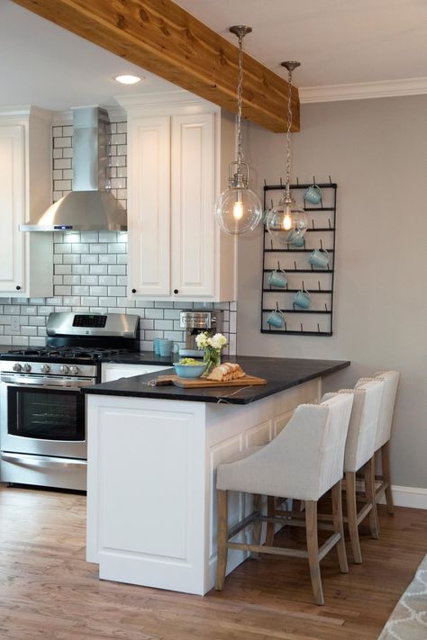 Fixer Upper hosts Chip and Joanna Gaines installed a natural wood support beam above the breakfast bar. All new white cabinets and black marble countertops bring a modern look to the kitchen, and two hanging globe light fixtures illuminate the breakfast bar. A new stainless steel range and vent hood is surrounded by a beveled subway tile backsplash to complete the stylish look. Black Marble Countertops, Kitchen Peninsula, Trendy Kitchen, Kitchen Redo, Kitchen Remodel Idea, Wood Kitchen, White Cabinets, Kitchen Colors, Dream Kitchen