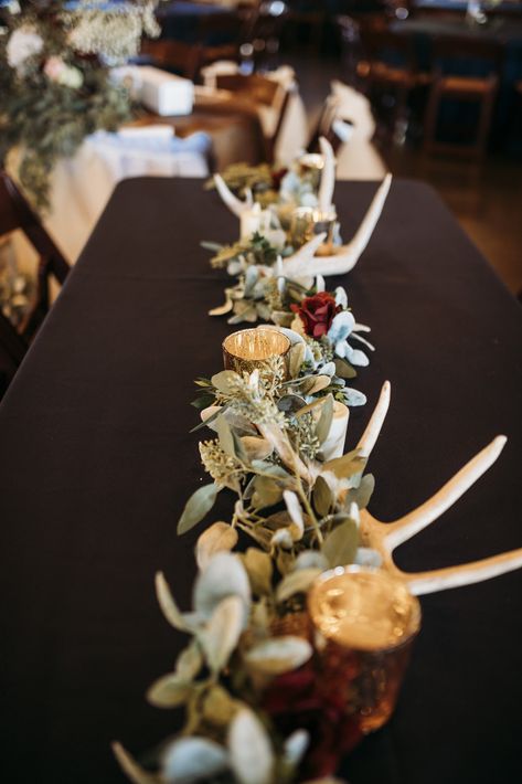 | long wedding table centerpiece with gold, maroon, + antlers | rustic elegant wedding centerpiece with antlers | elegant country wedding centerpiece ideas with antlers | winter country wedding decor ideas | winter country wedding centerpiece ideas | southern wedding table centerpiece with antlers | photo taken at THE SPRINGS Event Venue. follow this pin to our website for more information, or to book your free tour! SPRINGS location: Norman, OK photographer: Two Sticks Photography #weddingdecor Rustic Wedding Decor Antlers, Rustic Western Wedding Reception, Wedding Country Table Decorations, Rustic Hunting Wedding Decor, Rustic Lodge Wedding Decor, Deer Themed Wedding Ideas, Antler Bouquet Wedding Flowers, Antler And Greenery Centerpiece, December Country Wedding