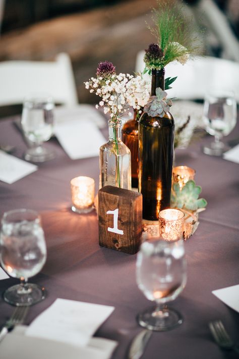 vintage wine bottle centerpiece idea Wedding Centerpieces Bottles, Bourbon Bottle Wedding Centerpieces, Wine Bottle Table Decor, Bourbon Bottle Centerpiece, Whiskey Bottle Centerpiece, Wine Bottle Wedding Decor, Wine Bottle Table Numbers, Wine Bottle Centerpiece, Wine Bottle Wedding Centerpieces