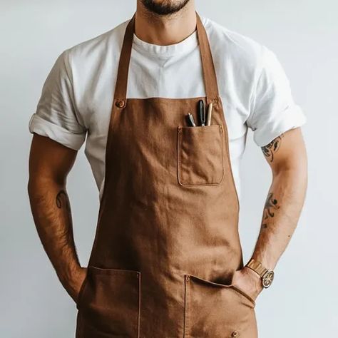 ↑↑↑ Larger size on website 🔸 A man wearing a white t-shirt and a brown apron stands with his hands in his pockets. He has a watch Tattoos On Both Arms, Man In White Shirt, Men Apron, Brown Apron, Artist Apron, Plain Background, Plains Background, Aprons For Men, Low Angle