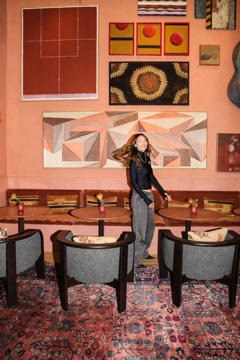 Kelly Wearstler Interiors - Restaurant Interior Design: In this image, Kelly Wearstler stands in Dahlia, the restaurant and cocktail lounge that she designed for the Downtown LA Proper Hotel. The space features vintage rugs, black idning room chairs, decorative pillows, painted walls in a pink shade and wall art. The pink wall has colorful wallpaper, colorful wall art, and abstract painting. Tap the pin to explore more of this space and for more restaurant design and restaurant aesthetic. Africa Interior Design, Kelly Wearstler Wallpaper, Kelly Wearstler Interiors, Proper Hotel, Restaurant Aesthetic, Wallpaper Colorful, Cocktail Lounge, Earring Inspo, Painted Walls