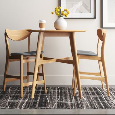 Inspired by iconic mid-century silhouettes, this 3-piece dining set creates a cohesive and minimal look in your kitchen or dining room. It includes a counter-height table and two stools, all crafted from solid and engineered wood with a light, natural oak finish that complements any modern space. The table is built on top of splayed legs with X-shaped support, and its round table top is designed to accommodate two guests after assembly. Both stools showcase curved backrests and built-in footrest Small Round Kitchen Table, Small Breakfast Table, Modern Kitchen Stools, Small Round Dining Table, Round Bar Table, Round Kitchen Table, Small Kitchen Tables, Small Apartment Kitchen, 3 Piece Dining Set