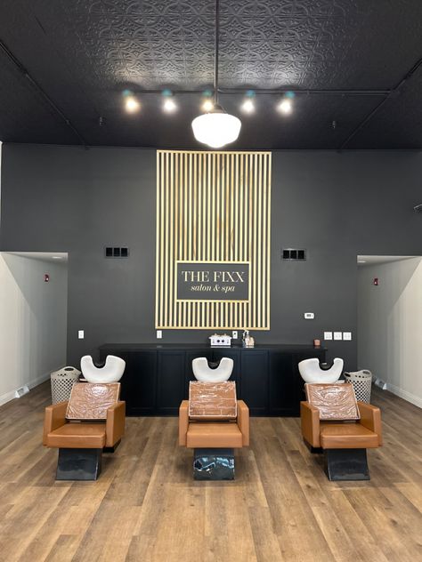 Black wall with vertical poplar wood slats, creating an accent wall. In the center, it says “THE FIXX SALON & SPA” Accent Wall For Salon Suite, Hair Salon Feature Wall, Salon With Black Walls, Salon Suite Accent Wall Ideas, Salon Picture Wall Ideas, Black Accent Wall Salon, Black And Wood Salon Decor, Black Wall Salon, Hair Salon Accent Wall