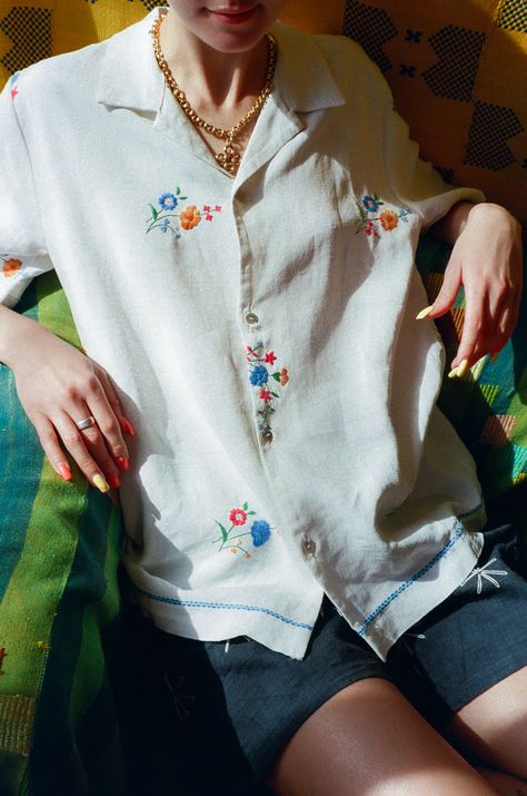 Short sleeve antique linen shirt in soft white with Madeira embroidery of little flower bouquets in blue, orange, and green. Boxy fit and camp collar. 4 mother of pearl button closure. Features special light x dark blue embroidered trim above and around the bottom hem. The majority of Behen's pieces are made either with very delicate fabrics and techniques or with antique textiles. All wear, mending, and idiosyncrasies are unique to the original fabric and are considered signs of love. Measurements (laying flat): Size Medium: Bust 43, Waist 43, Length 29, Shoulder 17.5, Sleeve 83/4 Michael is 5'9 with a 28" waist, and wears size medium with the Rock Jeans in Nonna. Laurence is 5'8 with a 27" waist, and wears size medium with the Linen Shorts in Soller and Vigna Necklace. Material: 100% lin Shirt Flower Embroidery, Flower Embroidery On Shirt, Embroidered Linen Top, Floral Embroidery Shirt, Embroidered Shirt Collar, Embroidery White Shirt, Button Up Embroidery, Embroidered White Shirt, Embroidery Shirt Ideas