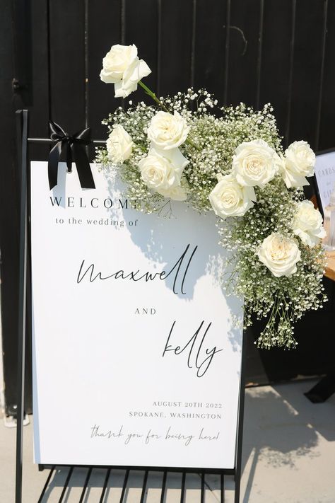 Classy welcome sign adorned by upper right corner baby's breath and white rose design. Welcome Wedding Sign Flowers, Baby’s Breath And White Rose Centerpieces, White Roses Baby’s Breath Centerpiece, Wedding Easel Flowers, Wedding Signs Flowers, White Wedding Ideas Decoration, Wedding Sign Flower Arrangement, White Rose And Baby’s Breath, Baby Breathe Weddings