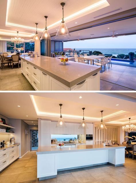 In this modern kitchen, a long white and grey island sits below three glass pendant lights that are hung from a recessed ceiling with hidden lighting. The kitchen faces the pool and views the expansive ocean. Kitchen With Sea View, Surf House Decor Interior Design, Grey Island, Grey Kitchen Island, Hidden Lighting, Glass Pendant Lights, Shore House, The Beach House, Mood Lights