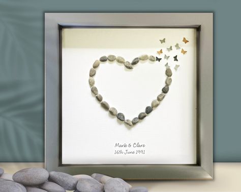 "A beautiful Personalised Wedding, Engagement or Anniversary picture gift of a Heart made from beach Pebbles, with coordinating butterflies, in a frame.  Your picture:  - Mounted in a 9 inch frame, you can choose from Grey, Black, White or Rustic wood.  Each frame is ready to hang on a wall - White, Black and White frames will stand alone o a shelf but Rustic wood frames are wall mounting only. - Any wording can be added to your picture. - Your picture will be boxed before it is carefully packaged for posting. How to order: 1.  Select whether you would like to see a 'proof photo' of your finished picture before it goes in the mail, 2.  Choose your frame colour 3.  \"Add to basket\" and leave a message in the 'personalisation box' to let me know the wording you would like added. 🤍 I can us Anniversary Frame, Beach Pebbles, Wall White, Anniversary Pictures, Beach Glass Art, Pebble Pictures, White Frames, Rustic Wood Frame, Picture Gifts