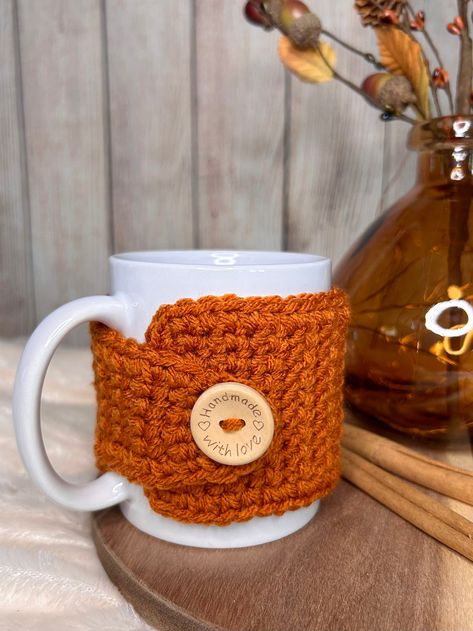 Snuggle up your coffee cup during cozy sweater weather with this handmade pumpkin spice crochet mug cozy. Perfect for 12 oz mugs, it keeps your hands from burning while keeping your drink warm. Plus, the 25mm natural wood button adds a heartfelt touch, saying "handmade with love." It arrives charmingly packaged, perfect for gifting and stuffing into stockings! SIZE: 3" wide x 12.25" longFits 12 oz (3.35"W x 3.94"H) mug Christmas Coffee Cozy, Crochet Mug Cozies, Christmas Crochet Cup Cozy, Crochet Christmas Cup Cozy, Coffee Cup Cozy Crochet Pattern Free, Knit Mug Cozy, Mug Crochet, Knit Coffee Cozy, Crochet Materials