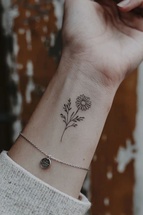 Flower tattoo on a wrist with a silver bracelet. Daisy Finger Tattoo Simple, Small Simple Nature Tattoos, First Tattoo Ideas Female, Small Nature Tattoos For Women, Tiny Wrist Tattoos For Women, Coverup Wrist Tattoos For Women, Small Wrist Tattoos For Women, Charming Tattoo, Small Nature Tattoo