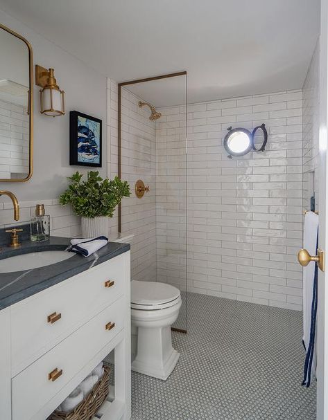 Placed on white penny floor tiles accented with gray grout, a white washstand is accented with a slatted shelf, brass hardware, and a honed black marble countertop holding an oval sink beneath an brass gooseneck faucet. Nautical Bathroom Decor Ideas, Seaside Bathroom Decor, Penny Tile Bathroom, Penny Tile Floor, Penny Tiles Bathroom, Penny Tile Floors, Beach Style Bathroom, Nautical Bathroom, White Bathroom Designs