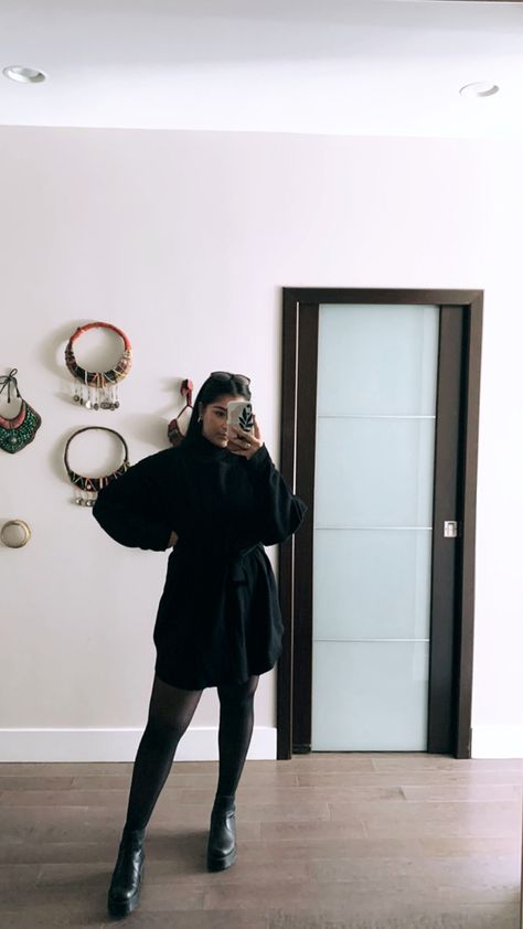 Indian girl taking a mirror selfie of her outfit that consists of black sweater dress with tie wasit, turtleneck underneath, sheer tights and doc marten boots and gold jewelry. Black Sweater Dress With Tights And Boots, Black Dress With Sheer Tights, Shirt Dress And Tights Outfit, Black Dress With Boots Winter, Black Sheer Tights Outfit, Black Dress With Black Tights, Black Dress And Tights Outfit, Dress With Turtleneck Underneath, Black Dress With Tights