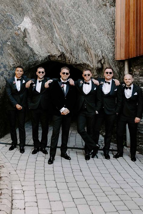 Grooms party wearing matching classic black-tie tuxedos, bow ties and grooms sunglasses | Becky Tranter Photography Groomsmen Sunglasses Photo, Groomsmen Attire Spring Wedding, Groomsmen Outfits Black, Tuxedo For Groomsmen, Black Tie Groomsmen, Wedding Photoshoot Beach, Black Tie Beach Wedding, Black Tie Wedding Party, Wedding Groomsmen Suits