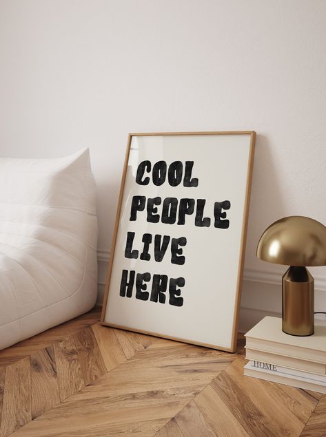 Add a fun and modern touch to your space with this "Cool People Live Here" typography wall art. Featuring bold black text in a minimalist design, this Scandinavian-inspired poster is perfect for creating an inviting atmosphere in any room. The clean, stylish font and uplifting message make it an ideal addition to your living room, entryway, or office. With its high-quality print and contemporary look, this poster celebrates positive vibes and cool spaces in a subtle yet impactful way. Cool People Live Here Poster, Typography Wall Art, Black Text Poster, Uplifting Wall Art, Minimalist Poster, Living Room Decor, Scandinavian Art Print, High Quality Wall Art, Fun Home Decor, Modern Typography Art, Positive Message Print, Stylish Wall Art, Contemporary Home Decor, Minimalist Black Poster, Tren Wall Art Living Room Minimalist, Living Room Minimalist, Room Minimalist, Scandinavian Art Print, Text Poster, Trendy Wall Decor, Cool People, Print Typography, Office Poster