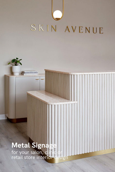 Minimalist and elegant reception area featuring the golden lettered 'SKIN AVENUE' sign above a cream-colored reception desk with vertical fluting and a modern, circular pendant light overhead Beauty Salon Room, Esthetician Room Decor, Esthetics Room, Spa Interior Design, Esthetician Room, Clinic Interior Design, Spa Interior, Salon Suites, Dental Office Design